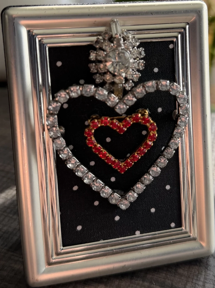 A small rectangular silver frame containing a rhinestone heart arrangement over black fabric with white dots.